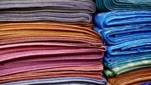 Tecidos coloridos arrumados e dobrados um em cima do outro, formando uma pilha de tecidos.